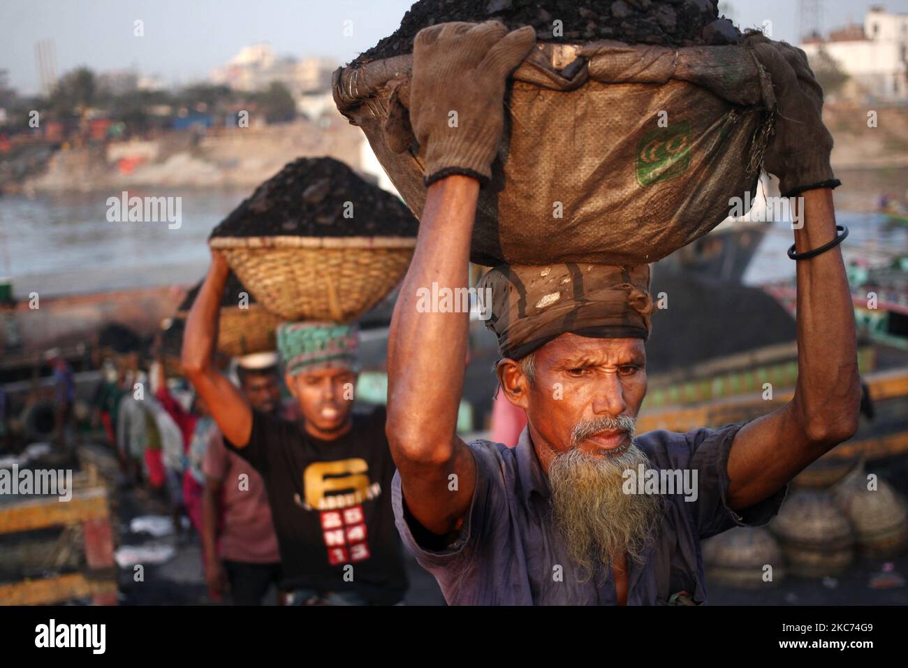 Les travailleurs transportent du charbon sur des paniers lorsqu'ils déchargent ces produits d'un cargo sur la rive du fleuve Buriganga à Dhaka, au Bangladesh, vendredi, au 08 janvier 2021. La consommation actuelle de charbon pour la production d'électricité est d'environ 3,5 millions de tonnes par an pour les deux centrales à charbon du Bangladesh, l'une à Barapukuria (440MW) à Dinajpur et l'autre est la nouvelle centrale Payra (660MW) à Patuakhali. Selon le rapport des médias, si le Plan directeur du secteur de l'énergie 2016 est mis en œuvre, la consommation de charbon pour la production d'électricité serait 10 fois plus en 2030 et 20 fois plus en 2041 que le rp Banque D'Images Les travailleurs transportent du charbon sur des paniers lorsqu'ils déchargent ces produits d'un cargo sur la rive du fleuve Buriganga à Dhaka, au Bangladesh, vendredi, au 08 janvier 2021. La consommation actuelle de charbon pour la production d'électricité est d'environ 3,5 millions de tonnes par an pour les deux centrales à charbon du Bangladesh, l'une à Barapukuria (440MW) à Dinajpur et l'autre est la nouvelle centrale Payra (660MW) à Patuakhali. Selon le rapport des médias, si le Plan directeur du secteur de l'énergie 2016 est mis en œuvre, la consommation de charbon pour la production d'électricité serait 10 fois plus en 2030 et 20 fois plus en 2041 que le rp Banque D'Images