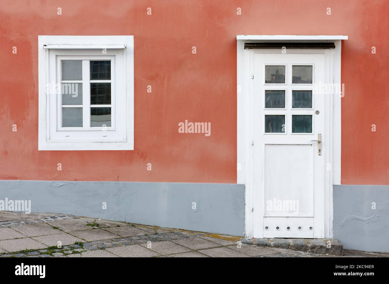 Détail de la façade d'un bâtiment avec le mur peint en orange et une porte et une fenêtre en blanc Banque D'Images