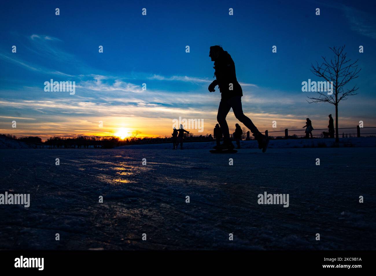Silhouettes sombres de personnes pendant le patinage sur glace sur le lac naturel gelé cristal dans la région du Brabant Nord dans l'après-midi avant le coucher du soleil. La frénésie du patinage sur glace prend le dessus des pays-Bas. Les Hollandais s'amusent et apprécient le temps enneigé froid d'une semaine avec des températures inférieures à zéro qui font geler les lacs, les ruisseaux, les étangs, les rivières et les canaux. La foule a été le patinage dans le parc Meerland près de la ville d'Eindhoven, pendant un ciel bleu ensoleillé jour, comme c'est une tradition hollandaise, les gens sont également vus à l'extérieur dans la nature glacée et l'environnement froid marchant sur la glace des lacs gelés, p Banque D'Images
