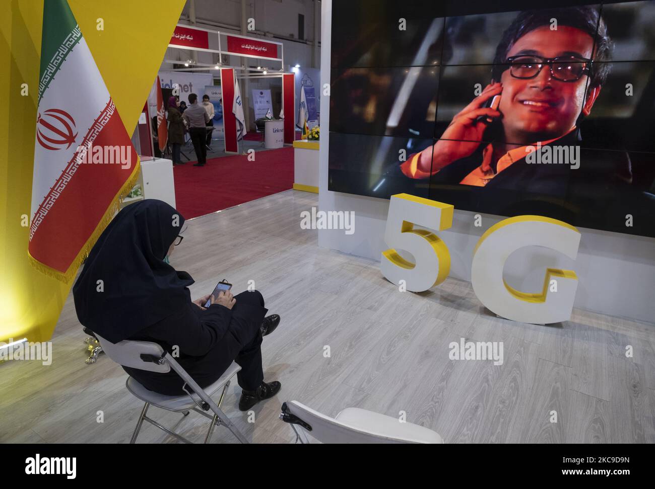 Un responsable iranien utilise son smartphone alors qu’elle se trouve à côté du logo 5G de la société de réseau mobile d’Irancell dans le stand de la sixième exposition iranienne sur l’Internet des objets (IoTex 2021) au Centre international d’exposition de Téhéran sur 16 février 2021. Le premier réseau 5G de l'Iran a été géré par la société Irancell, qui est une société iranienne de télécommunications qui exploite le plus grand réseau 2G-3G-4G-4,5G en Iran, également 5G réseaux mobiles et des services Internet fixes sans fil TD-LTE. (Photo de Morteza Nikoubazl/NurPhoto) Banque D'Images