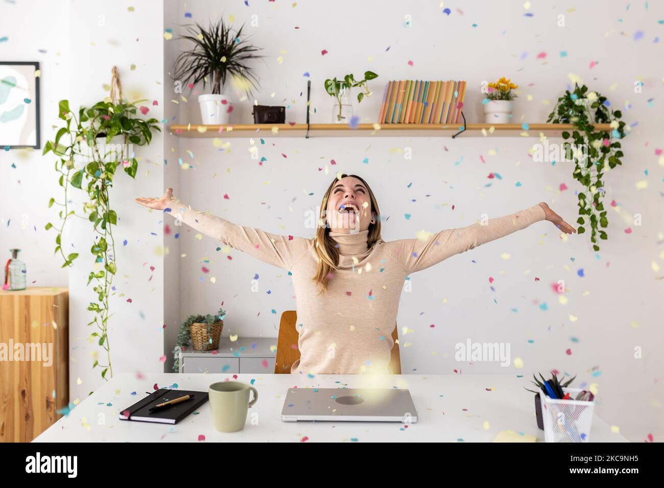 Jeune femme d'affaires célébrant le succès de jeter des confettis assis au bureau à domicile Banque D'Images
