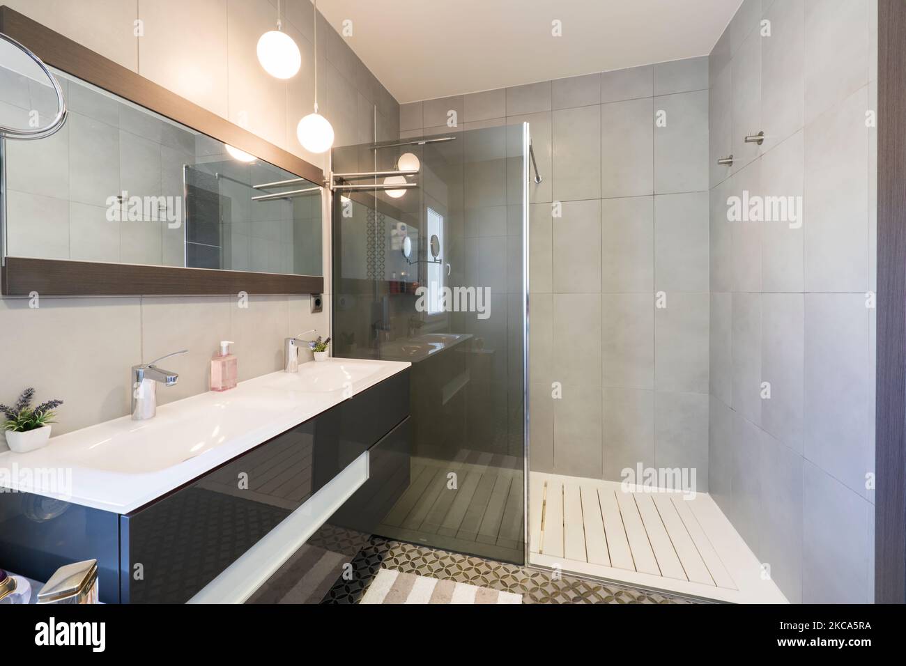 salle de bains avec miroir rectangulaire, meuble gris avec double lavabo blanc et cabine de douche avec cloison en verre gris Banque D'Images