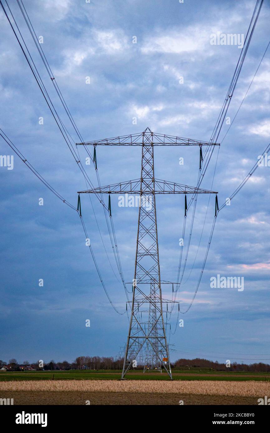 Poteaux électriques haute tension pendant l'heure magique. Les tours métalliques, vues au coucher du soleil dans la campagne hollandaise, distribuent l'énergie électrique de la centrale électrique, de la Belgique et de l'Allemagne à travers le pays. Les fils électriques, la grille et les piliers ou les pylônes de puissance sont vus comme des silhouettes dans le ciel nuageux et coloré de crépuscule. Stevensweert, pays-Bas sur 19 mars 2021 (photo de Nicolas Economou/NurPhoto) Banque D'Images