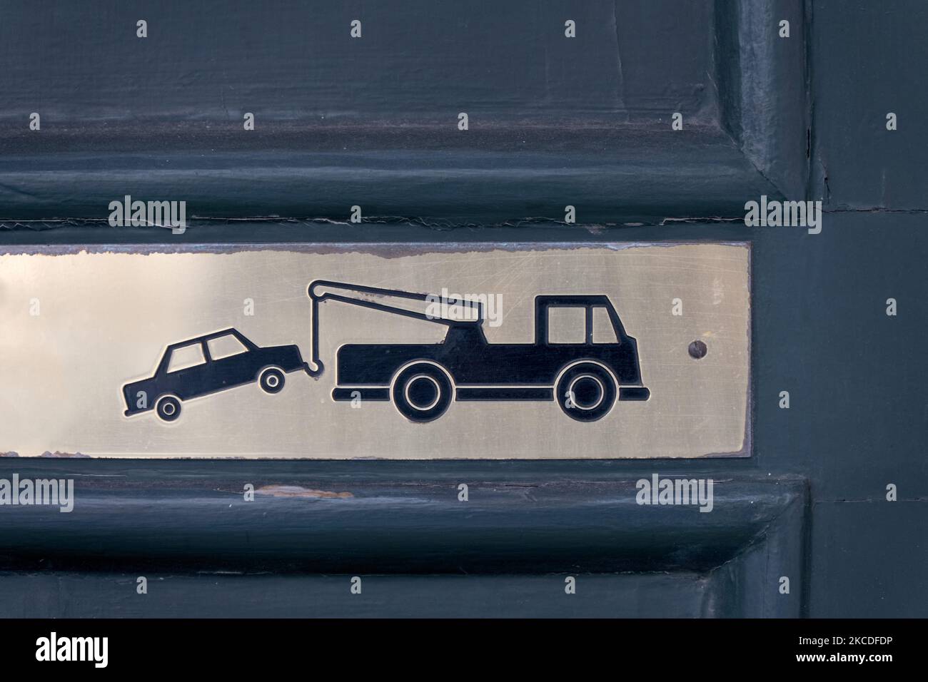 Vue rapprochée partielle de la barrière verte texturée avec panneau en laiton métallique monté sur celle-ci avec un camion de remorquage remorquant une voiture comme avis d'absence de stationnement et les zones à k Banque D'Images