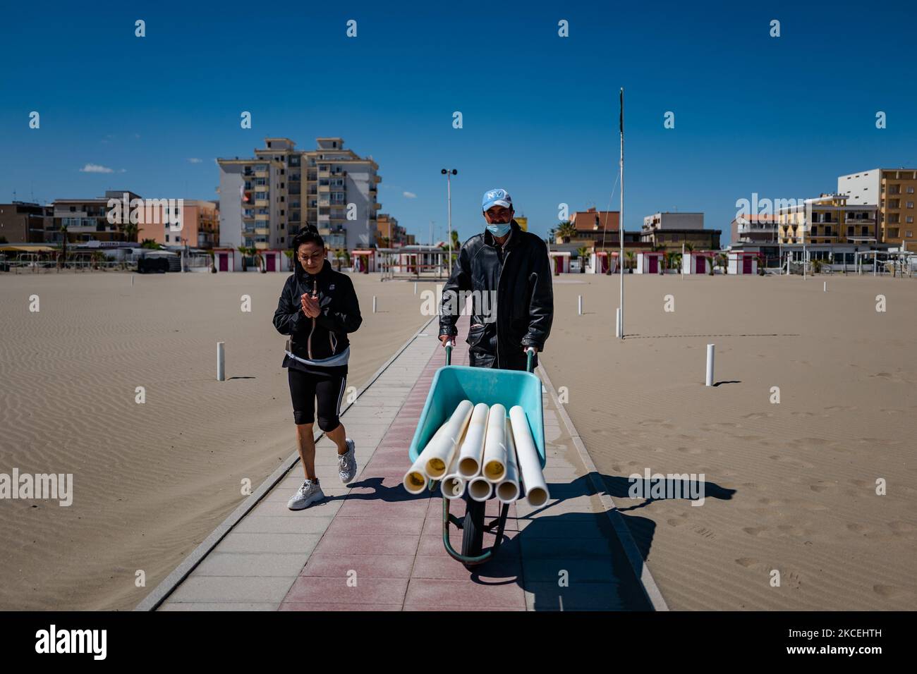 Un ouvrier transporte les bâtons pour les parasols sur la plage de Margherita di Savoia, Italie sur 14 mai 2021. Les directeurs des plages de baignade l'ont déjà fait, d'autres sont en train d'organiser des allées, des cabines, des belvédères et des bases pour les parasols tandis que pour ce qui concerne les plages publiques, Les municipalités ont commencé les travaux d'entretien des structures fixes et la remise en état avec l'enlèvement des déchets et des matériaux divers apportés par les tempêtes des mois d'hiver. La saison commencera officiellement le samedi 15 mai, plus tôt que par le passé, comme l'a établi l'ordonnance de baignade de 2021 de la Re Banque D'Images