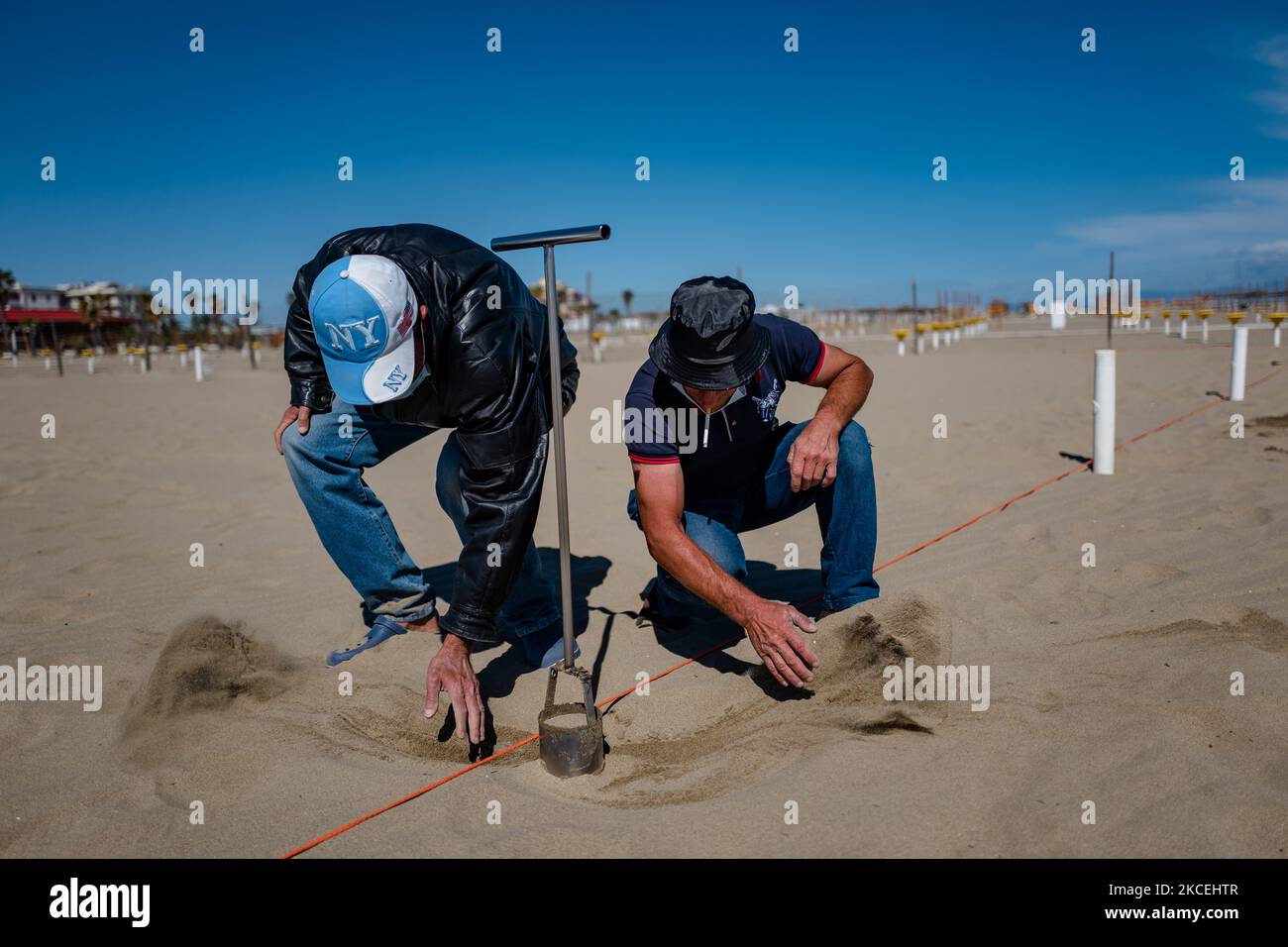 Les ouvriers placent les poteaux pour les parasols sur la plage de Margherita di Savoia, en Italie, sur 14 mai 2021. Les gestionnaires des plages de baignade l'ont déjà fait, d'autres sont en train d'organiser des allées, des cabines, Belvédères et bases pour parapluies alors que pour ce qui concerne les plages publiques les municipalités ont commencé les travaux d'entretien des structures fixes et la remise en état avec l'enlèvement des déchets et divers matériaux apportés par les tempêtes des mois d'hiver. La saison commencera officiellement le samedi 15 mai, plus tôt que par le passé, comme établi par l'ordonnance de baignade de 2021 de la région an Banque D'Images