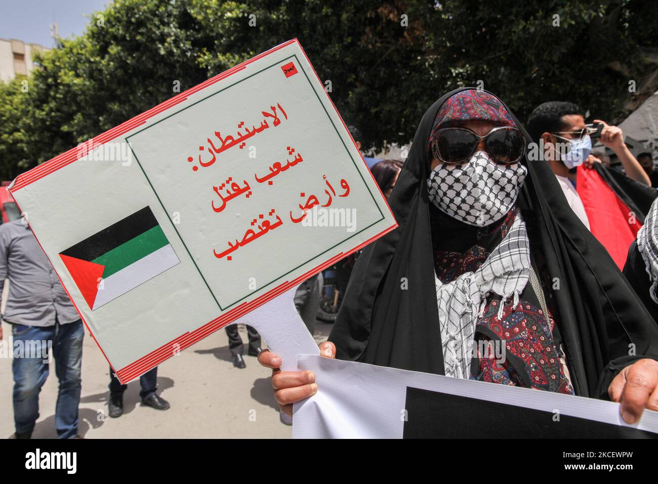 Une femme porte un écriteau qui lit en arabe, la colonie est Une personne tuée et une terre violée, lors d'une manifestation tenue devant le bâtiment du Parlement tunisien dans la ville de Bardo Tunis, en Tunisie, sur 18 mai 2021, D'appeler à l'adoption d'une loi par le Parlement, qui criminalise toutes les formes de normalisation des relations avec Israël. Les manifestants ont également protesté contre les frappes aériennes israéliennes dans la bande de Gaza ainsi que contre les violations israéliennes dans les territoires occupés en Palestine, en particulier dans le quartier palestinien Sheikh Jarrah à Jérusalem-est. La manifestation intervient après Banque D'Images