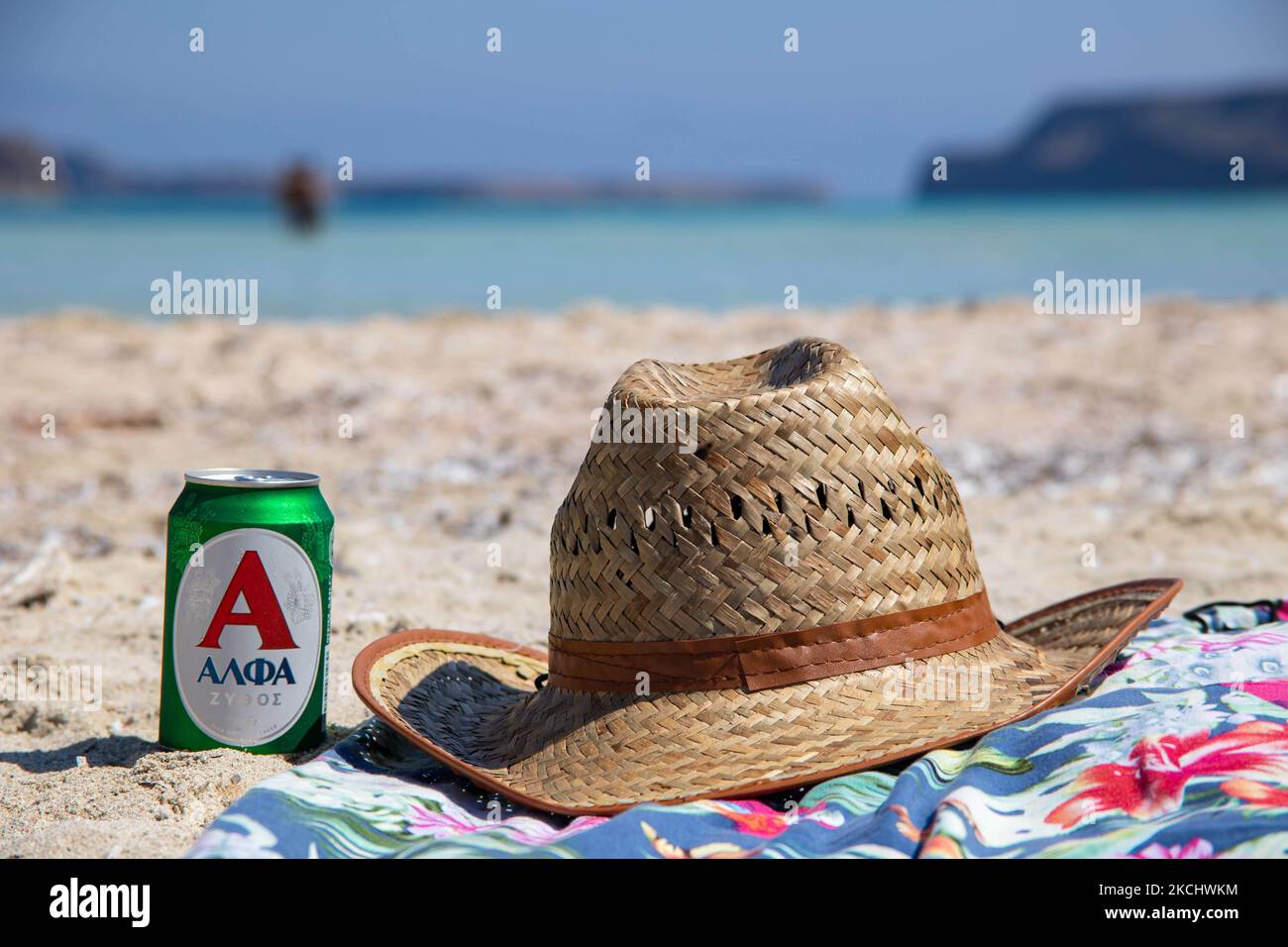 Un chapeau et une bière sur une serviette sur le sable de la plage de Balos, l'incroyable lagon avec les eaux turquoise exotiques et tropicales de la mer Méditerranée est situé dans la région de Chania, sur l'île de Crète. Balos est l'une des plages les plus visitées de Crète et est populaire auprès des visiteurs du monde entier. L'eau cristalline, le lagon, les montagnes rocheuses escarpées, un bar de plage fournissant des parasols et l'ombre avec des boissons et une île pirate sont situés dans la même région qui est accessible par une randonnée de 20 minutes ou bateau. La Grèce tente de stimuler son tourisme et de donner des privilèges pour se faire vacciner contre le coronavirus du Covid-19 PAN Banque D'Images