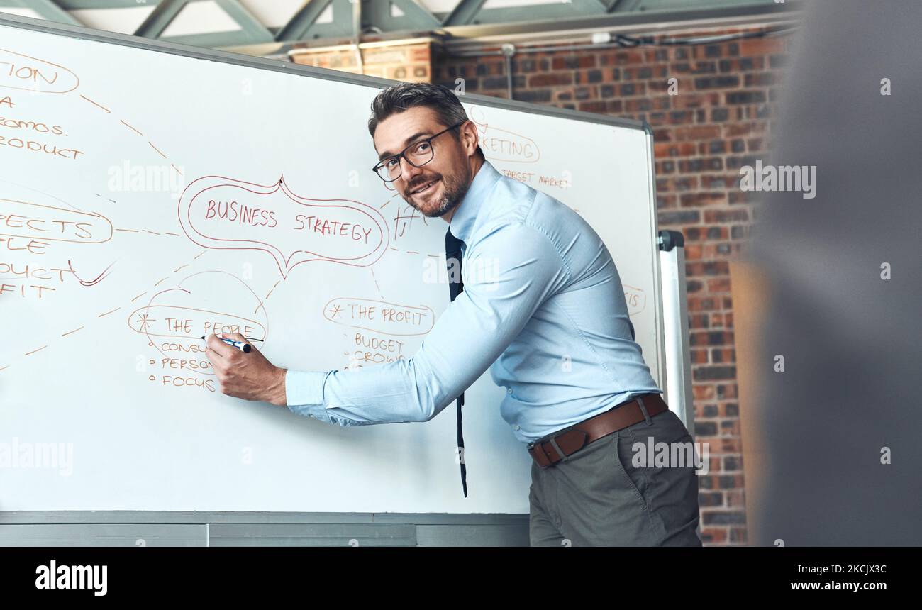 S'assurer que tout le monde comprend le plan global. Un homme d'affaires mature utilisant un tableau blanc pendant une présentation dans un bureau. Banque D'Images