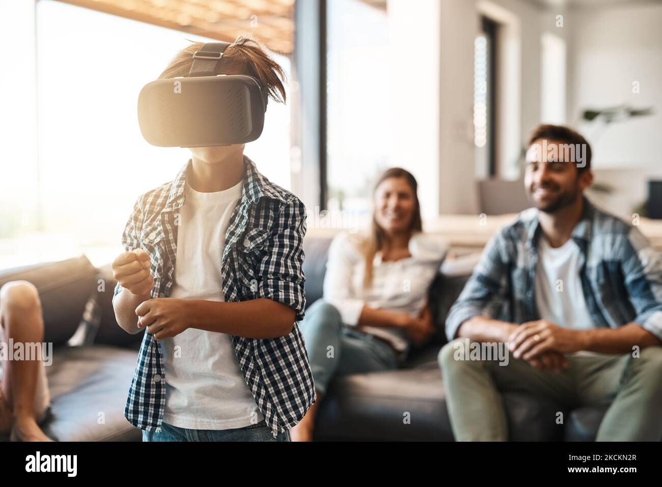 La réalité virtuelle pour la toute première fois. Un petit garçon utilisant un casque de réalité virtuelle à la maison avec ses parents en arrière-plan. Banque D'Images