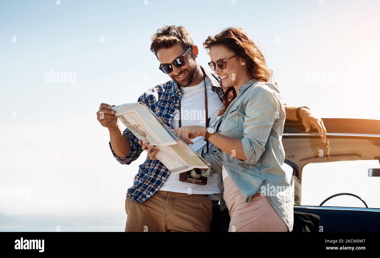 À la recherche des routes les moins fréquentées. Un couple affectueux qui regarde une carte tout en appréciant un voyage en voiture. Banque D'Images