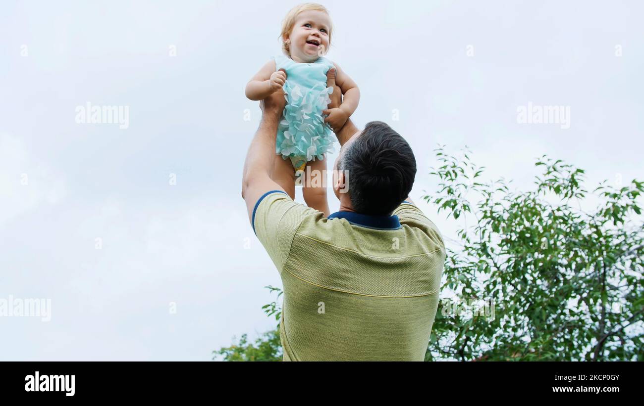 été, dans le jardin, la mère, une vue d'en dessous, le papa jette sa fille d'un an, joue avec elle, a du plaisir. Elle rit et la famille passe son temps libre ensemble. Photo de haute qualité Banque D'Images