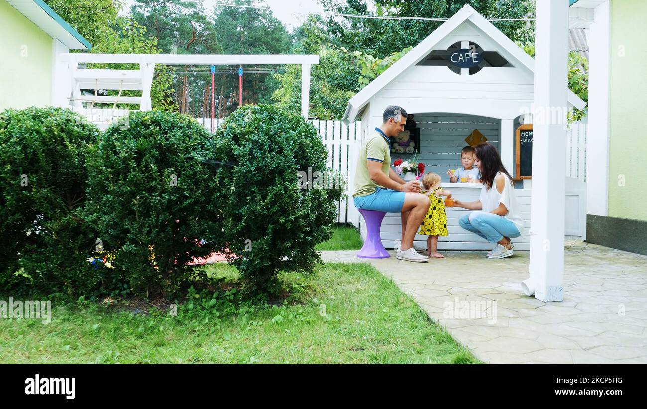 l'été, dans le jardin, les parents jouent avec de jeunes enfants, une fille et un garçon, dans un café, dans une salle de jeux pour enfants, traitent les enfants avec des jus de fruits fraîchement pressés, des jus de boisson. Photo de haute qualité Banque D'Images