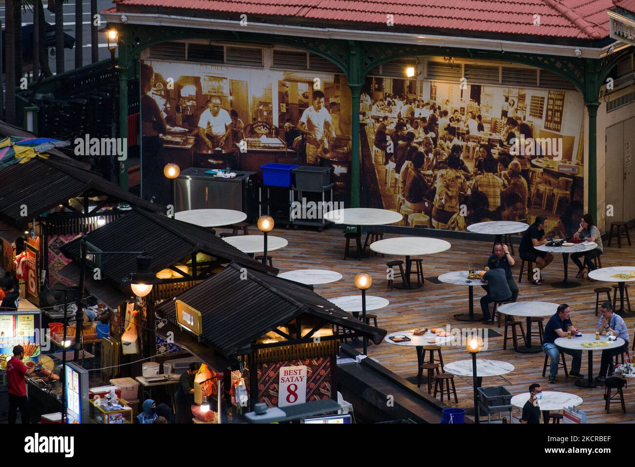 Les personnes assises par groupes de 2 personnes conformément aux restrictions de sécurité de Covid-19 dînent devant une affiche d'images d'archives dans un centre alimentaire de Singapour le samedi 23 octobre 2021. (Photo de Joseph Nair/NurPhoto) Banque D'Images