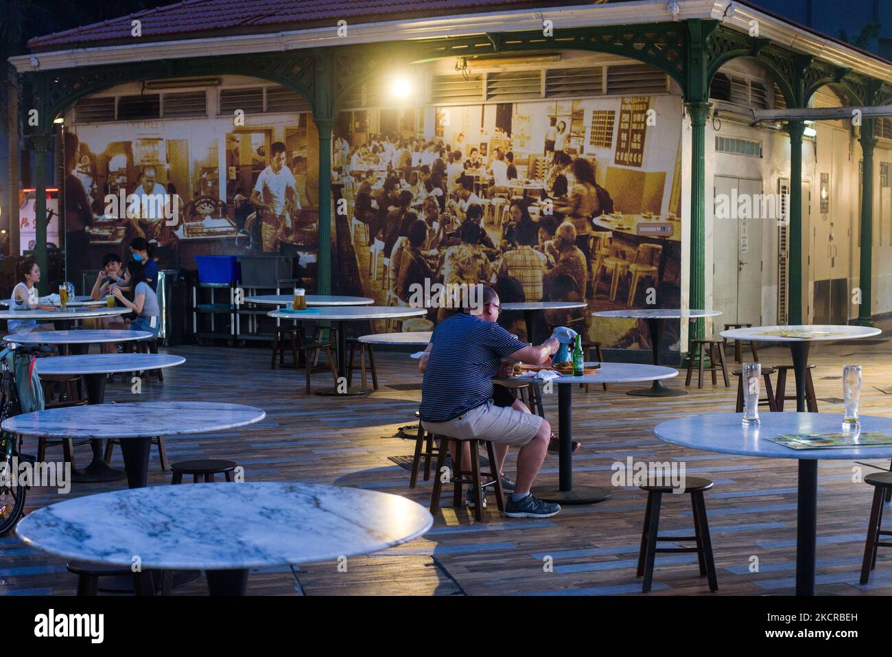 Les personnes assises à des tables par groupes de 2 personnes conformément aux restrictions de sécurité de Covid-19 dînent devant une image d'archives utilisée comme papier peint dans un centre alimentaire de Singapour le samedi 23 octobre 2021. (Photo de Joseph Nair/NurPhoto) Banque D'Images