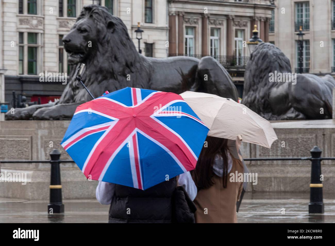 Cité de Westminster, Londres, Royaume-Uni. 5th novembre 2022. Le temps à Londres a été couvert et pleuvait. Les visiteurs sont toujours à l'extérieur de la vue sur les attractions. Touristes à Trafalgar Square avec drapeau Union Jack parapluie et statue de lion Banque D'Images