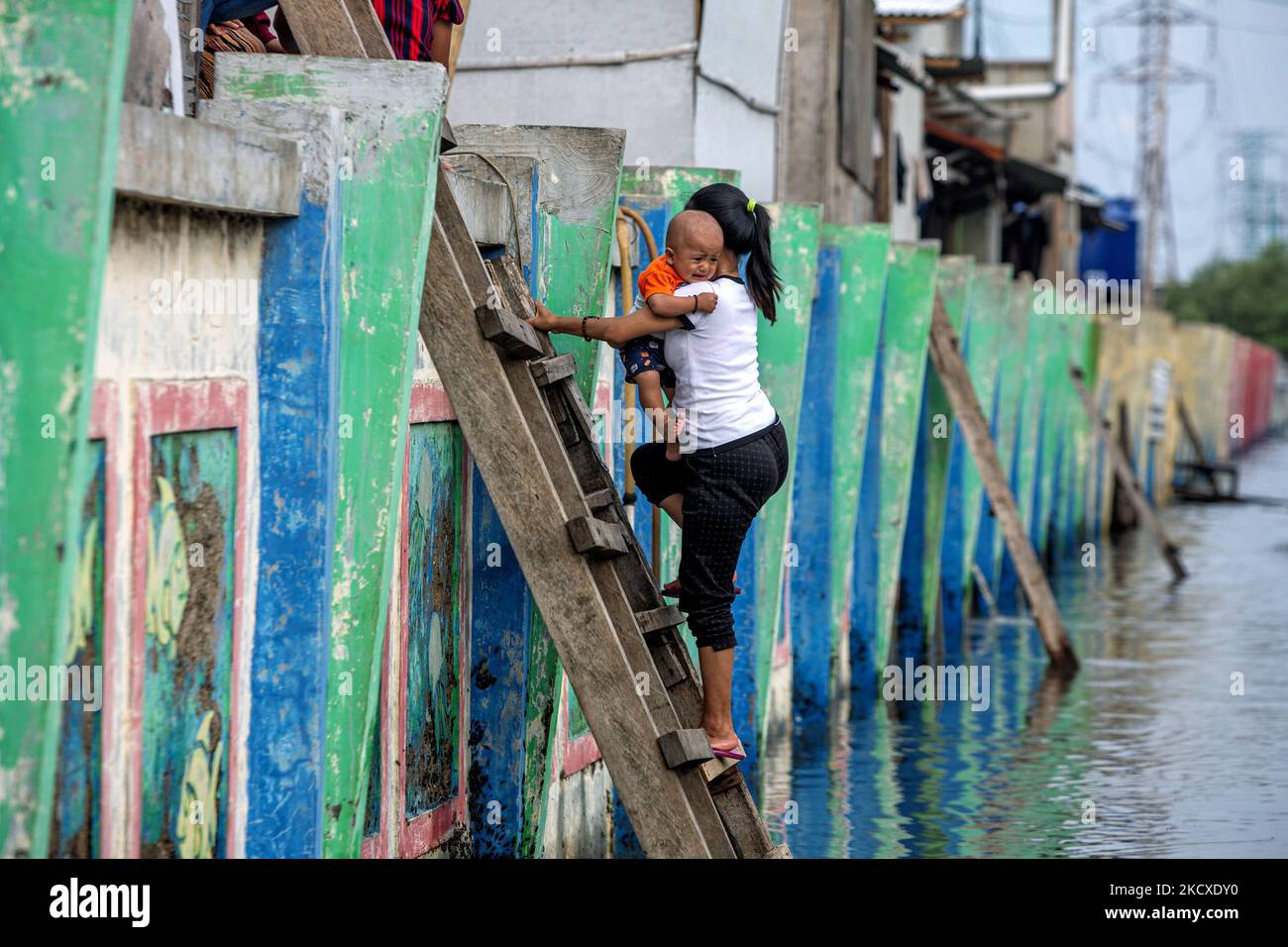 Une femme tient un bébé tout en montant des escaliers pour éviter les vagues de marée dans la zone côtière de Jakarta, Muara Angke, le 7 décembre 2021. Les autorités locales ont prédit que des marées et des vents violents frapperont la région de la baie de Jakarta et le nord de W. Java du 6 au 9 décembre, ce qui provoquerait l'immersion de la zone côtière de la capitale et endommagera les maisons. Les inondations causées par le débordement d'eau de mer ont submergé 15 unités de quartier dans le nord de Jakarta et l'ouest de Jakarta. (Photo par Afriadi Hikmal/NurPhoto) Banque D'Images