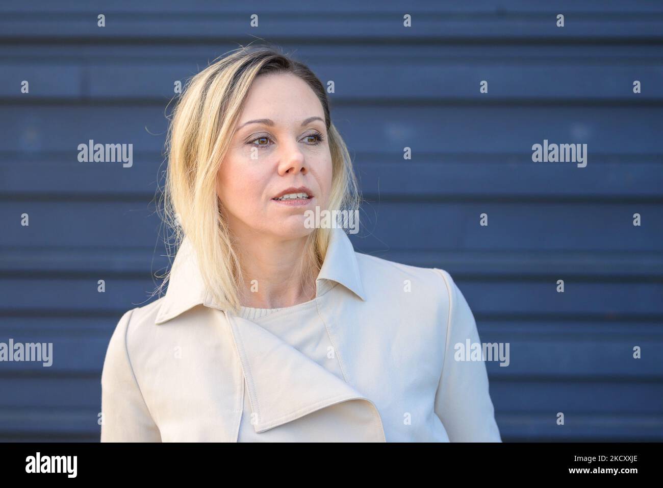 Portrait d'une jolie femme blonde d'âge moyen regardant soigneusement sur le côté devant un mur bleu Banque D'Images