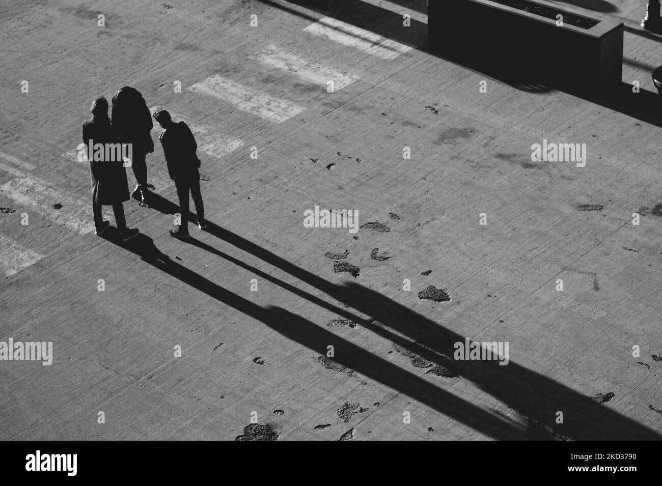 Photo en niveaux de gris de personnes debout et projetant des ombres allongées au milieu d'une rue Banque D'Images