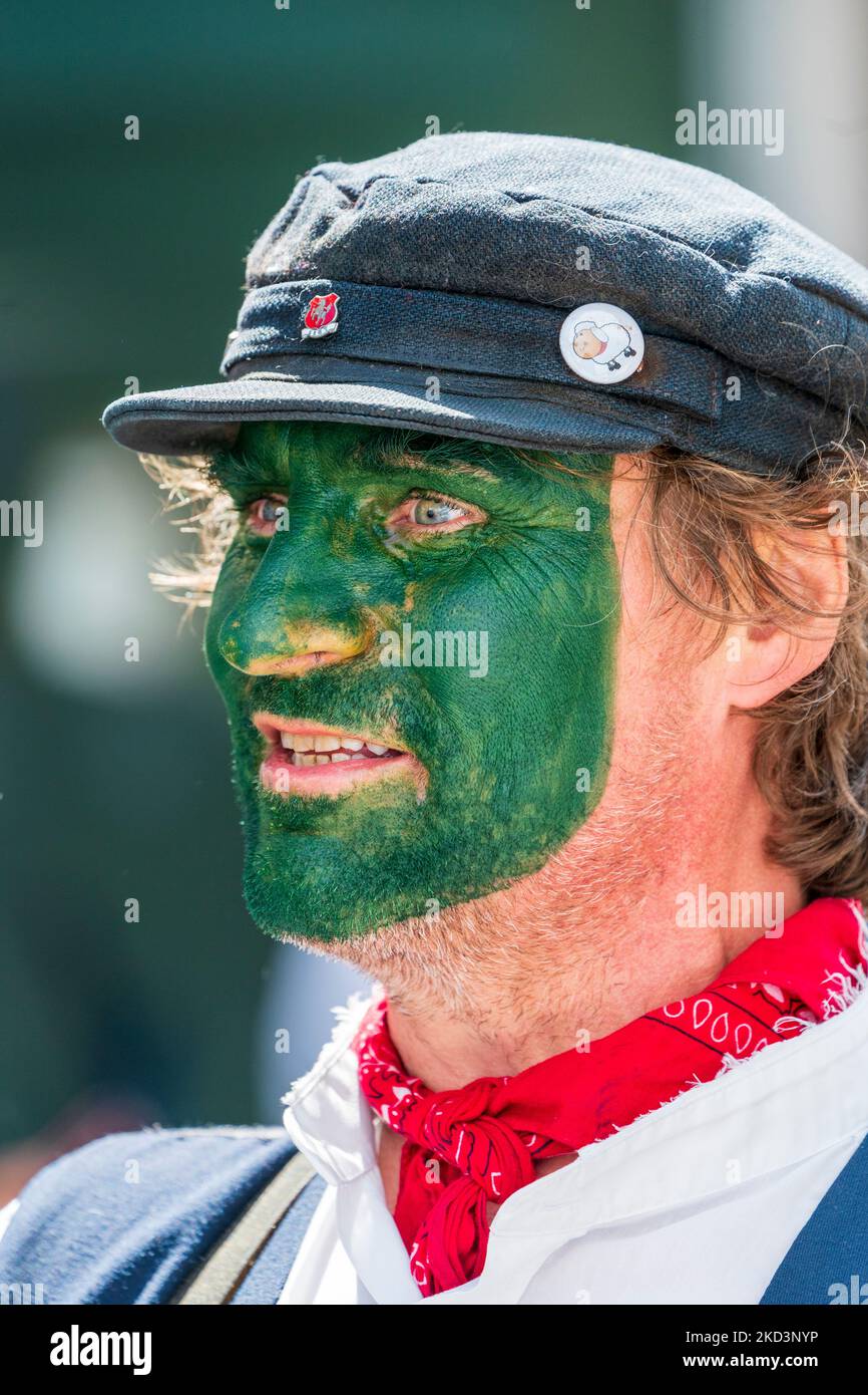 Gros plan sur le visage d'un danseur Morris de la piste Dead Horse Morris, avec un visage peint en vert et une casquette plate tout en dansant lors d'un événement en plein air. Banque D'Images