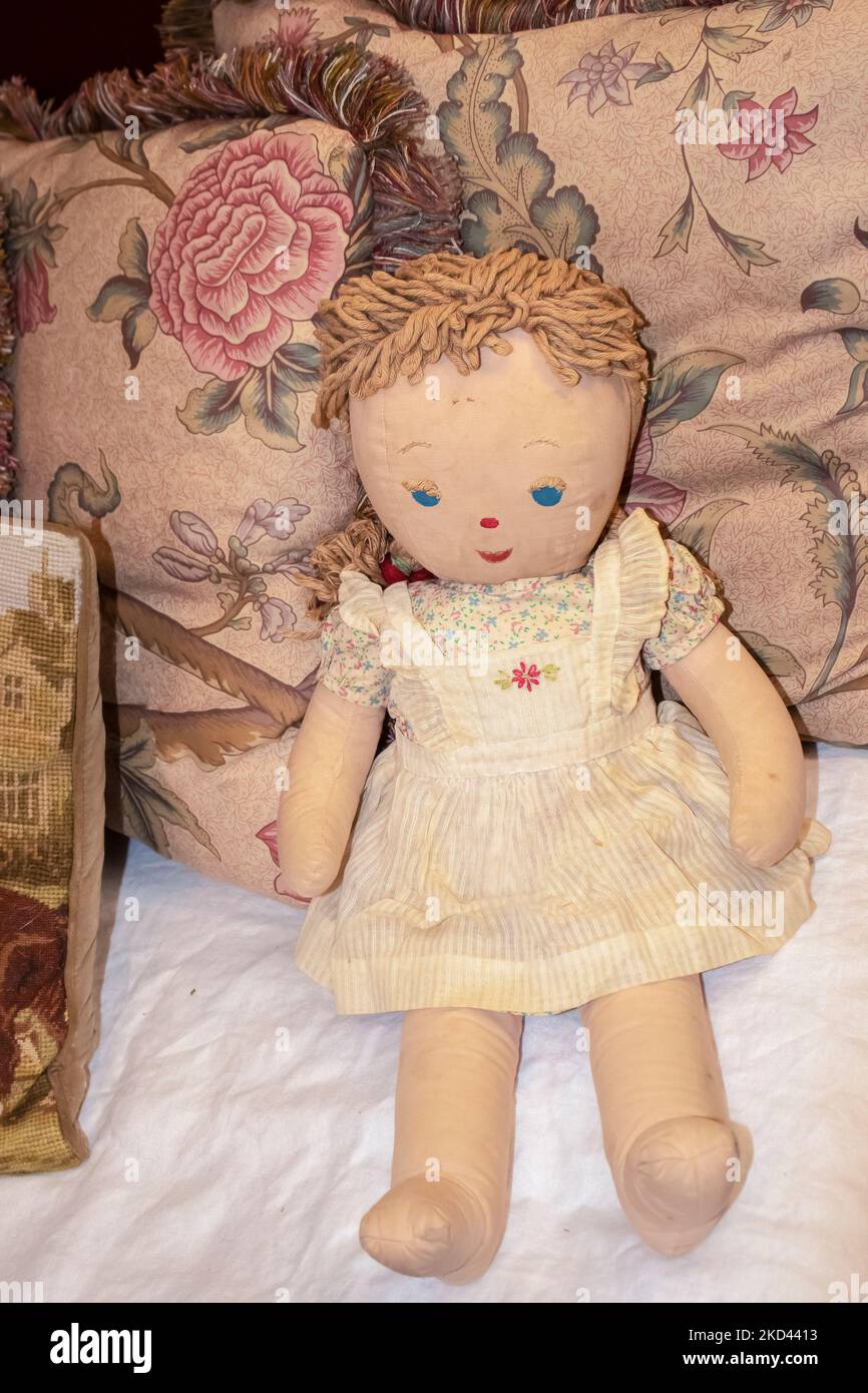 Vieille poupée de chiffon coloré avec les yeux et la bouche peints et brodés de brodearsucker pinapret appuyé contre des oreillers à franges florales - vintage Banque D'Images
