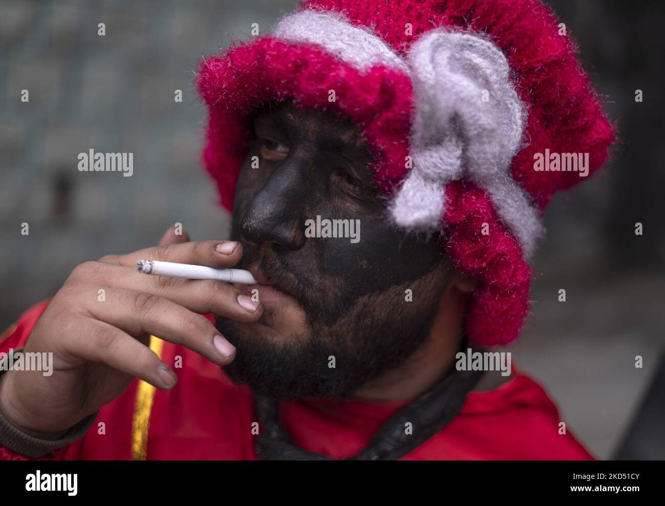 Un iranien peint son visage en noir et portant des robes rouges tandis que Hajji Firuz (un symbole du nouvel an iranien) fume alors qu’il se trouve dans la rue du nord de Téhéran sur 12 mars 2022. Hajji Firuz est un personnage fictif du folklore iranien qui apparaît dans les rues au début de Nowruz. Son visage est couvert de suie, et il est vêtu de vêtements rouge vif. Il danse dans les rues tout en chantant et en jouant de la musique. (Photo de Morteza Nikoubazl/NurPhoto) Banque D'Images