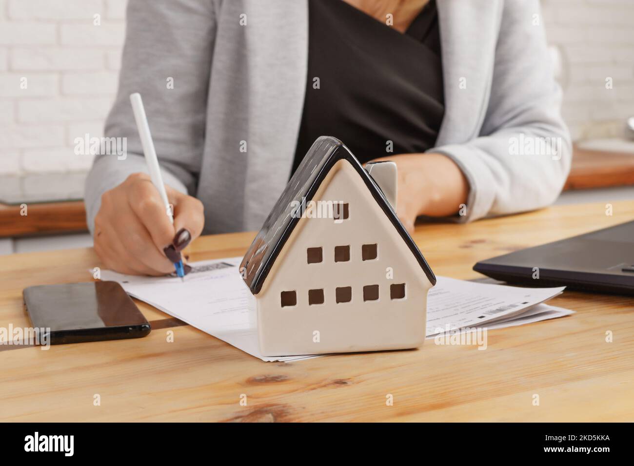 Une femme d'affaires signe des documents sur l'arrière-plan d'un modèle de maison contre l'arrière-plan de meubles de cuisine. Le concept d'acheter une maison, Mo Banque D'Images