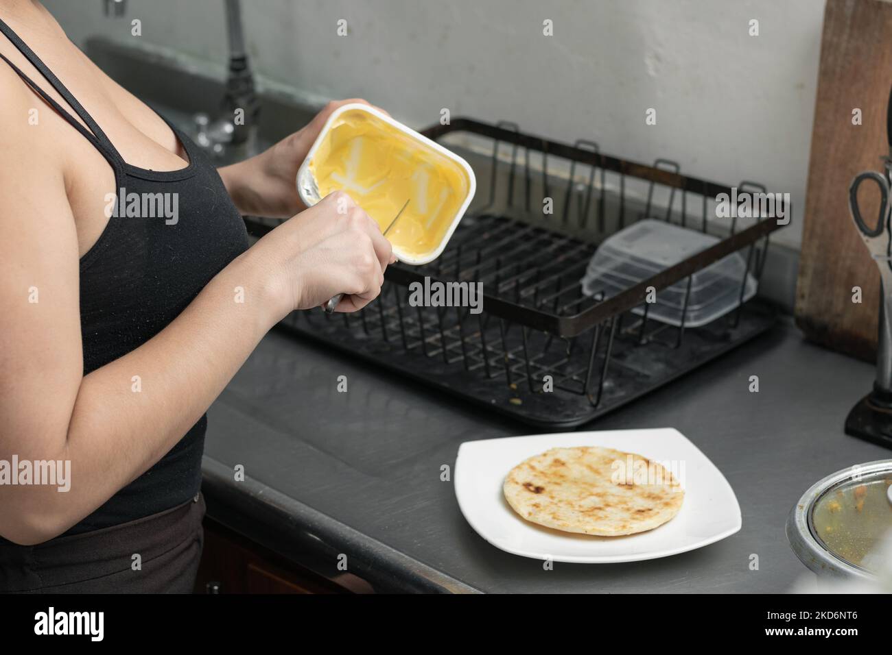 latina femme dans sa cuisine, enlever le beurre avec un couteau pour le verser dans l'arepa, préparant un petit déjeuner typiquement colombien. Banque D'Images