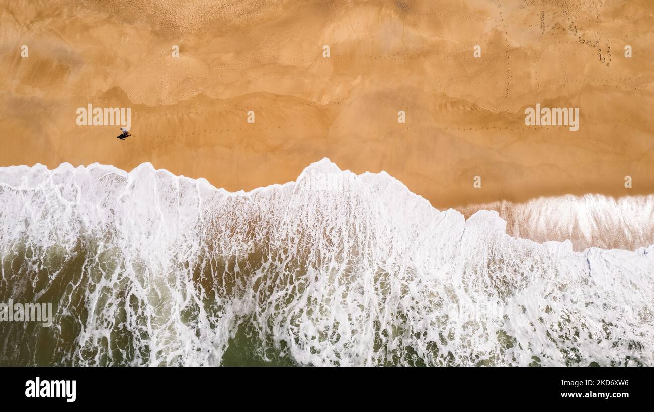 Vue d'un drone sur un homme qui marche sur la plage de Nazaré, au Portugal, sur 1 avril 2022. Nazaré, en particulier Praia do Norte ou North Beach, est célèbre pour les plus grandes vagues surfables de la planète. (Photo de Manuel Romano/NurPhoto) Banque D'Images