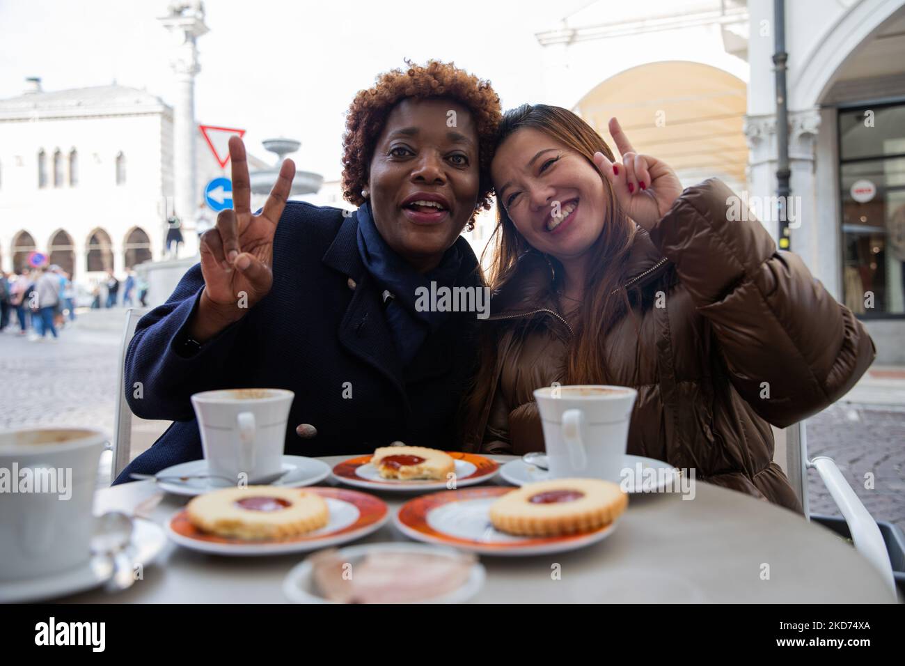 Deux amis multiraciaux souriants apprécient leur petit déjeuner pour faire un signe de victoire. Banque D'Images