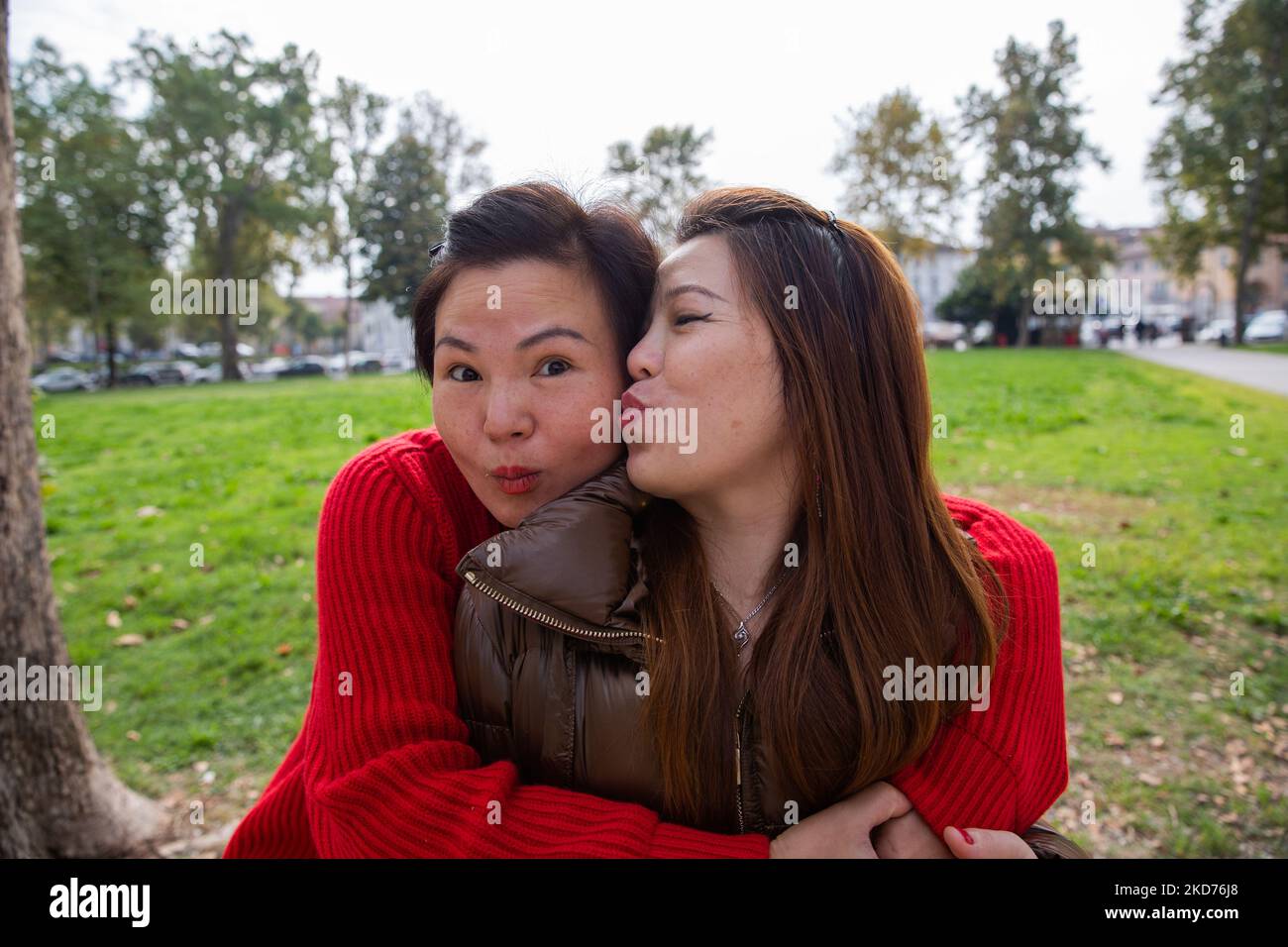 Deux amies chinoises qui s'embrasent dans le parc. L'un embrasse l'autre sur la joue. Banque D'Images