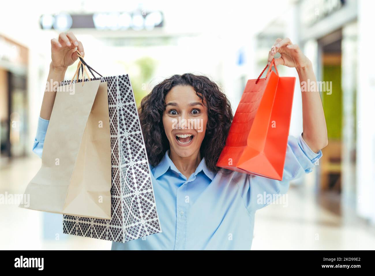 Portrait d'une femme heureuse shopper, femme hispanique dans un supermarché avec des sacs colorés est heureux et regardant l'appareil photo, à l'intérieur d'un grand magasin de vêtements Banque D'Images
