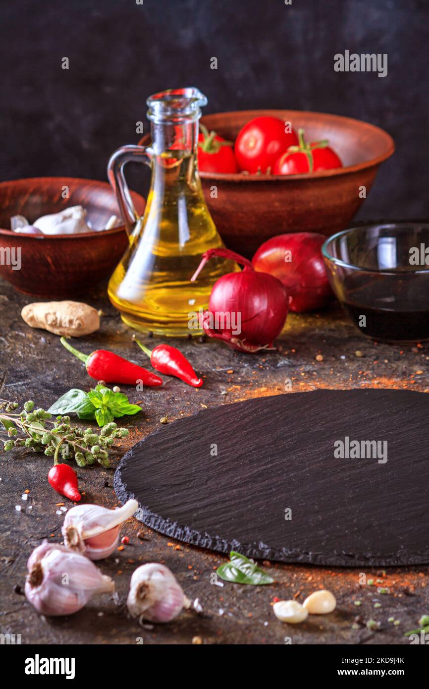 Décor culinaire avec table ronde en ardoise, huile d'olive dans une carafe et légumes.Espace vide pour le menu ou la recette avec mise au point sélective Banque D'Images