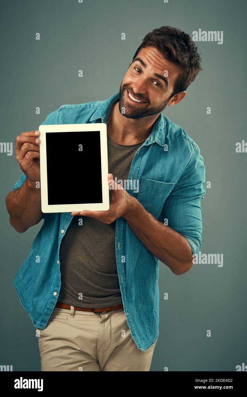 C'est assez incroyable, vous ne pensez pas. Portrait studio d'un jeune homme charmant tenant une tablette numérique avec un écran vierge sur fond gris. Banque D'Images