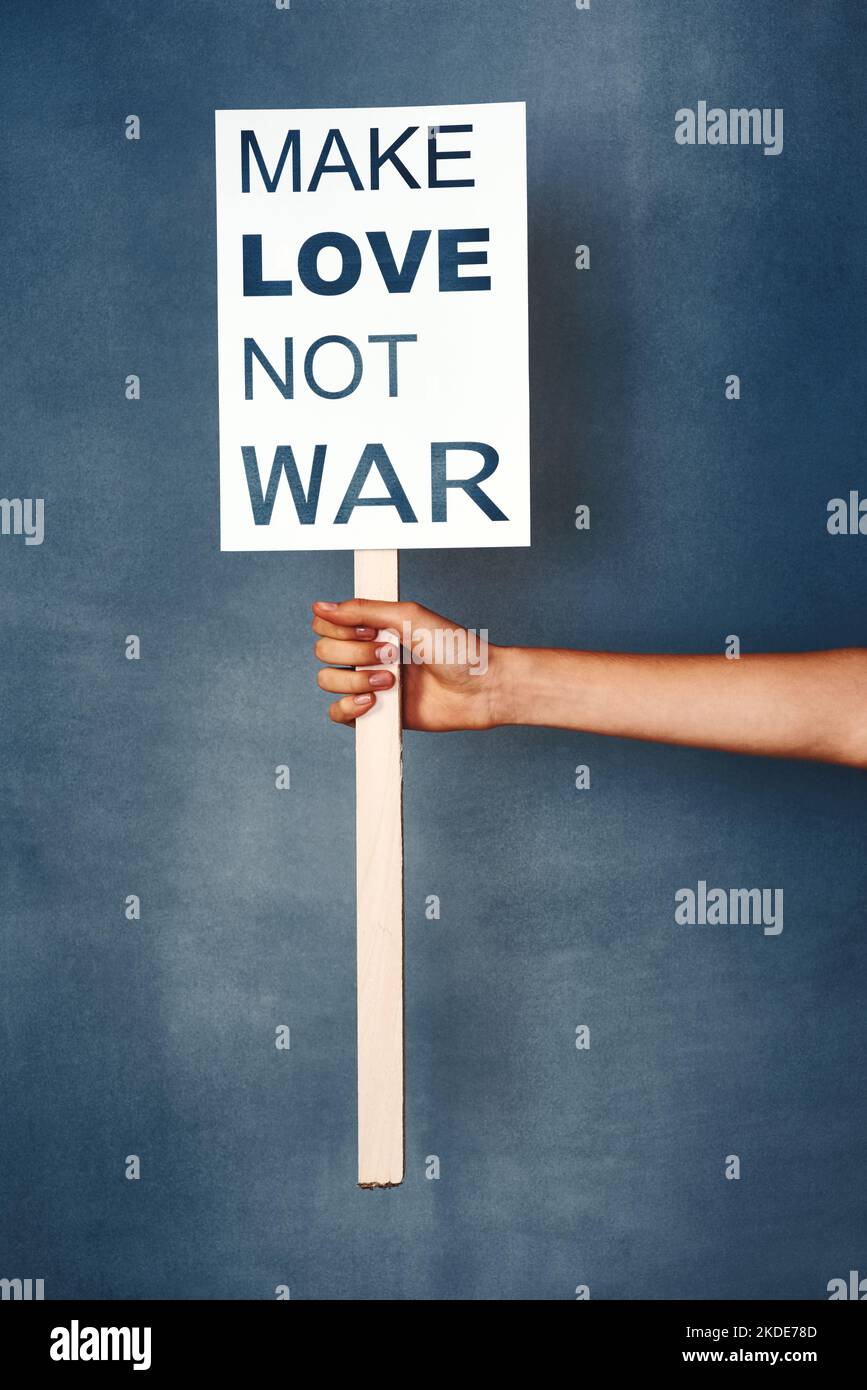 La paix est la seule voie. Studio photo d'une femme tenant un signe qui dit faire l'amour pas la guerre contre un fond bleu. Banque D'Images