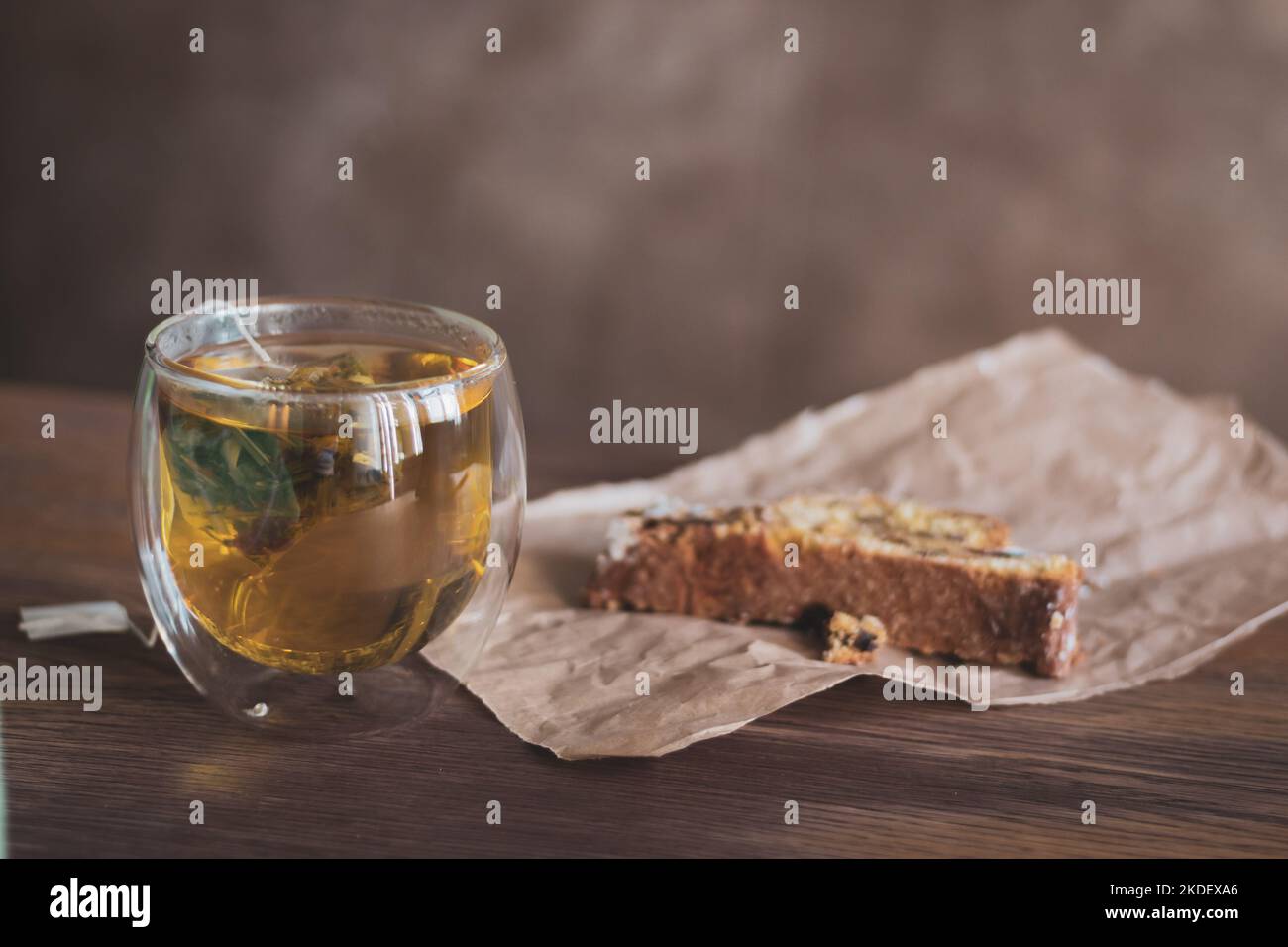 Tisane en verre et biscuit sur papier artisanal. Petit déjeuner confortable. Sachet de thé en verre avec gâteau. Boisson chaude et dessert. Boulangerie fraîche et thé au café. Banque D'Images