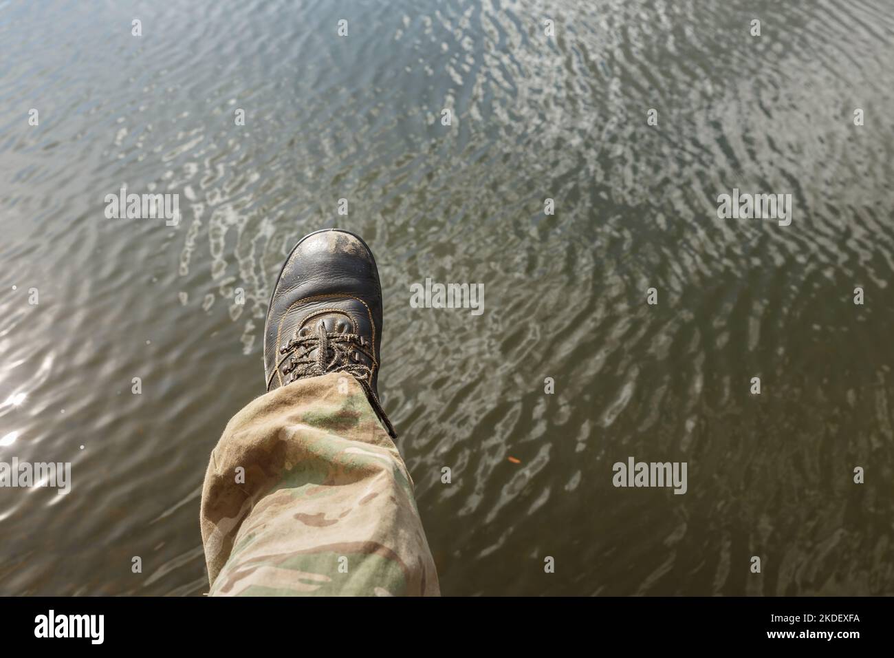 Partie basse de la personne au-dessus de l'eau. La jambe gauche d'un homme dans un pantalon de camouflage et de vieilles bottes se décale au-dessus de l'eau. Banque D'Images