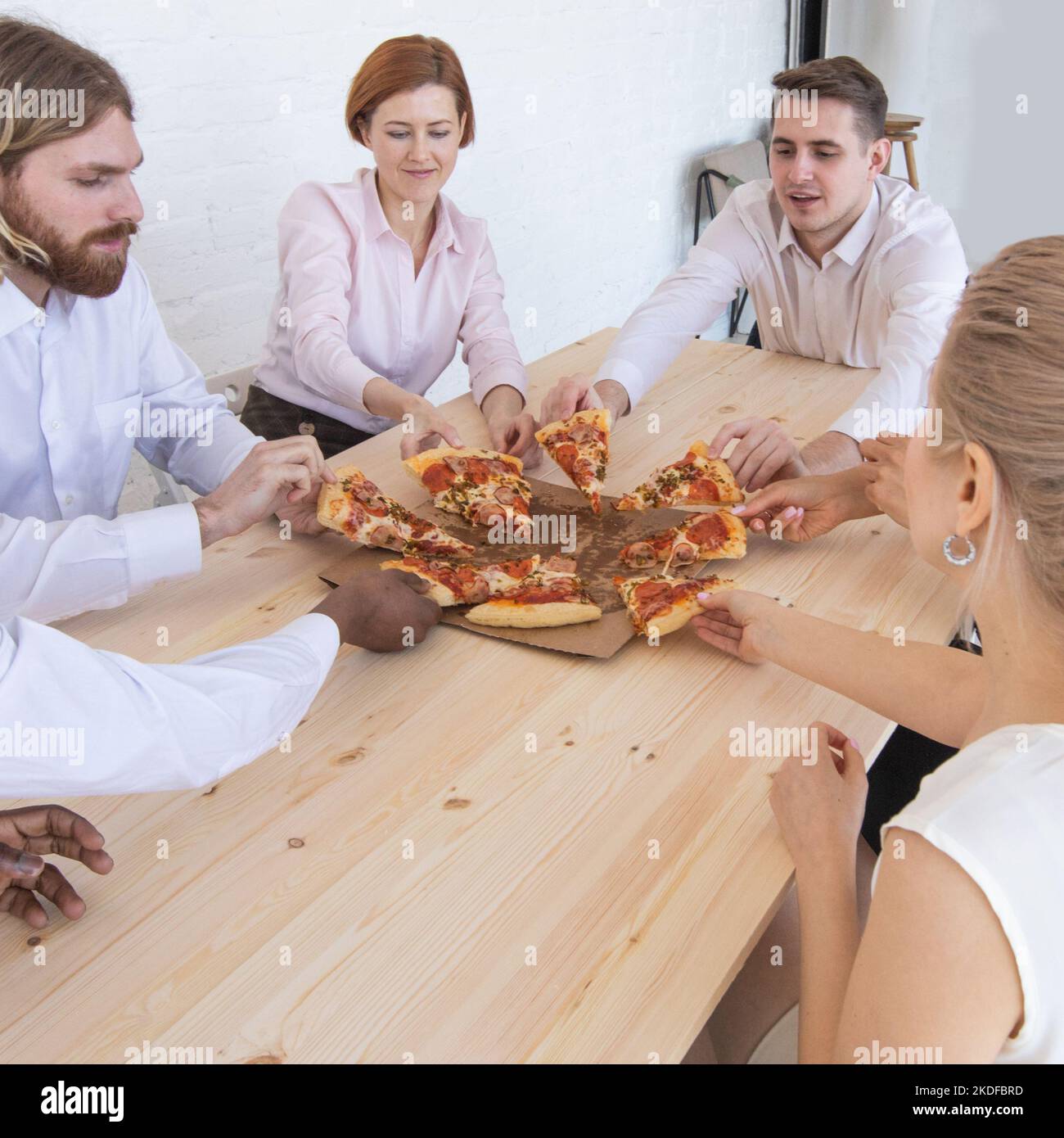 L'équipe d'affaires eating pizza in office assis autour de la table Banque D'Images