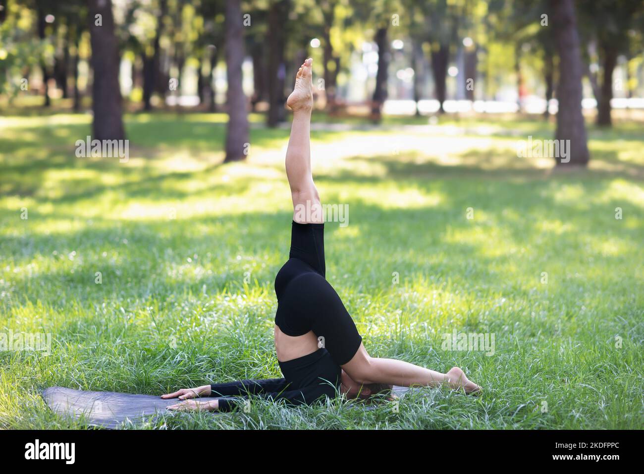 Femme pratiquant le yoga, faisant de l'exercice karnapidasana dans la salamba sarvangasana, s'exerçant sur un tapis dans le parc Banque D'Images