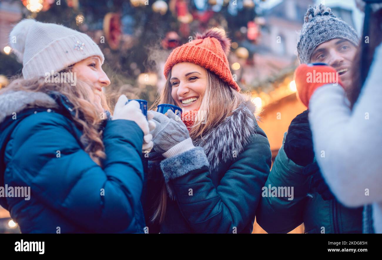 Groupe d'amis qui boivent du vin chaud dans le froid sur un marché de Noël Banque D'Images