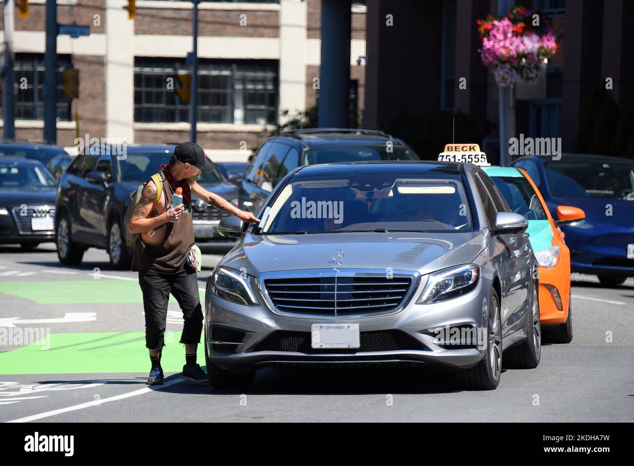 Toronto, Canada - 12 août 2022: Squegee homme essuie le pare-brise de Mercedes-Benz dans la circulation. Banque D'Images