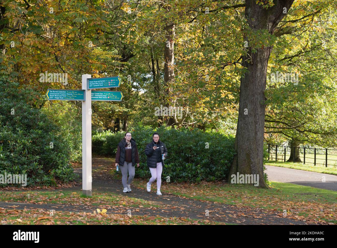 Deux visiteurs marchant devant un Signpost à Pollok Country Park, Glasgow, en automne Banque D'Images