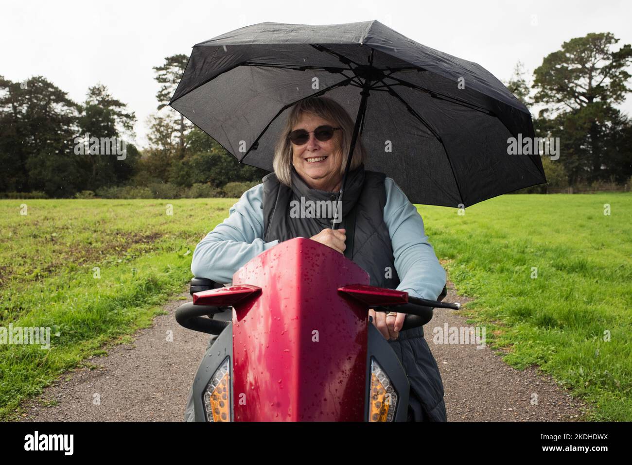 femme handicapée à la retraite sur un scooter de mobilité à l'extérieur sous la pluie Banque D'Images
