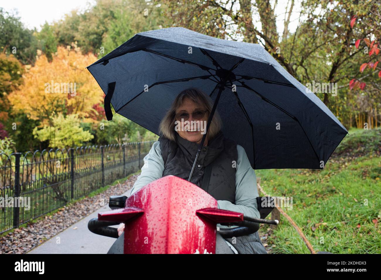 femme handicapée à la retraite sur un scooter de mobilité à l'extérieur sous la pluie Banque D'Images