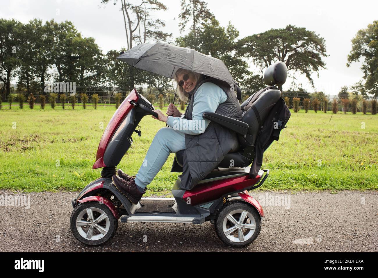 femme à la retraite sur un scooter de mobilité à l'extérieur sous la pluie Banque D'Images