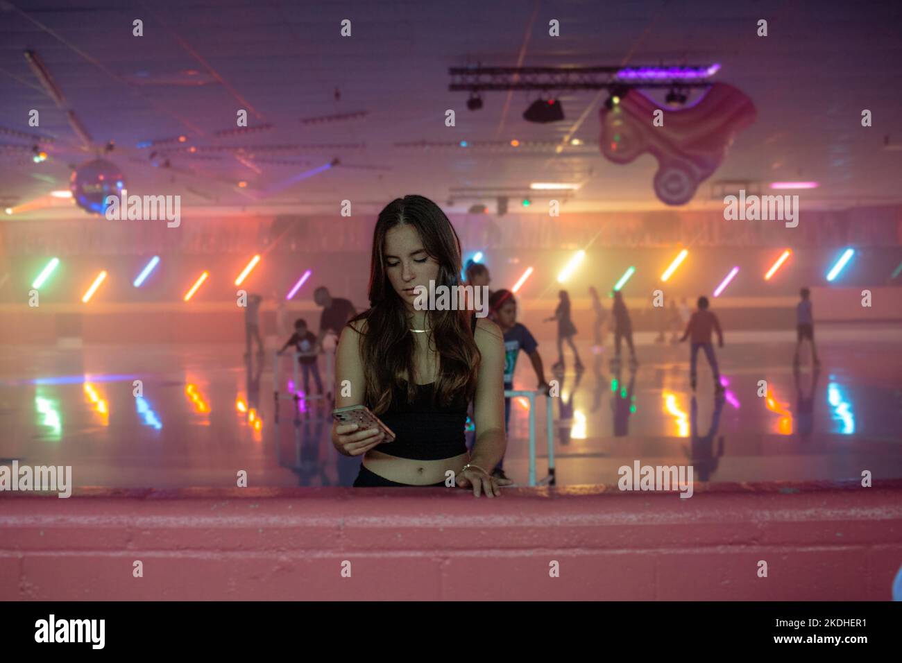 Une jeune fille vérifie son téléphone sur le côté de la patinoire Banque D'Images