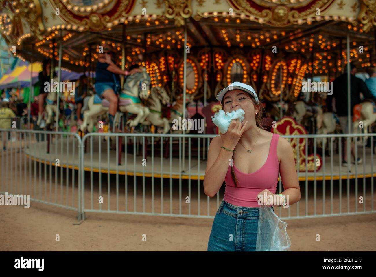 Adolescent mangeant une grosse boule de bonbons en coton devant un carrousel Banque D'Images