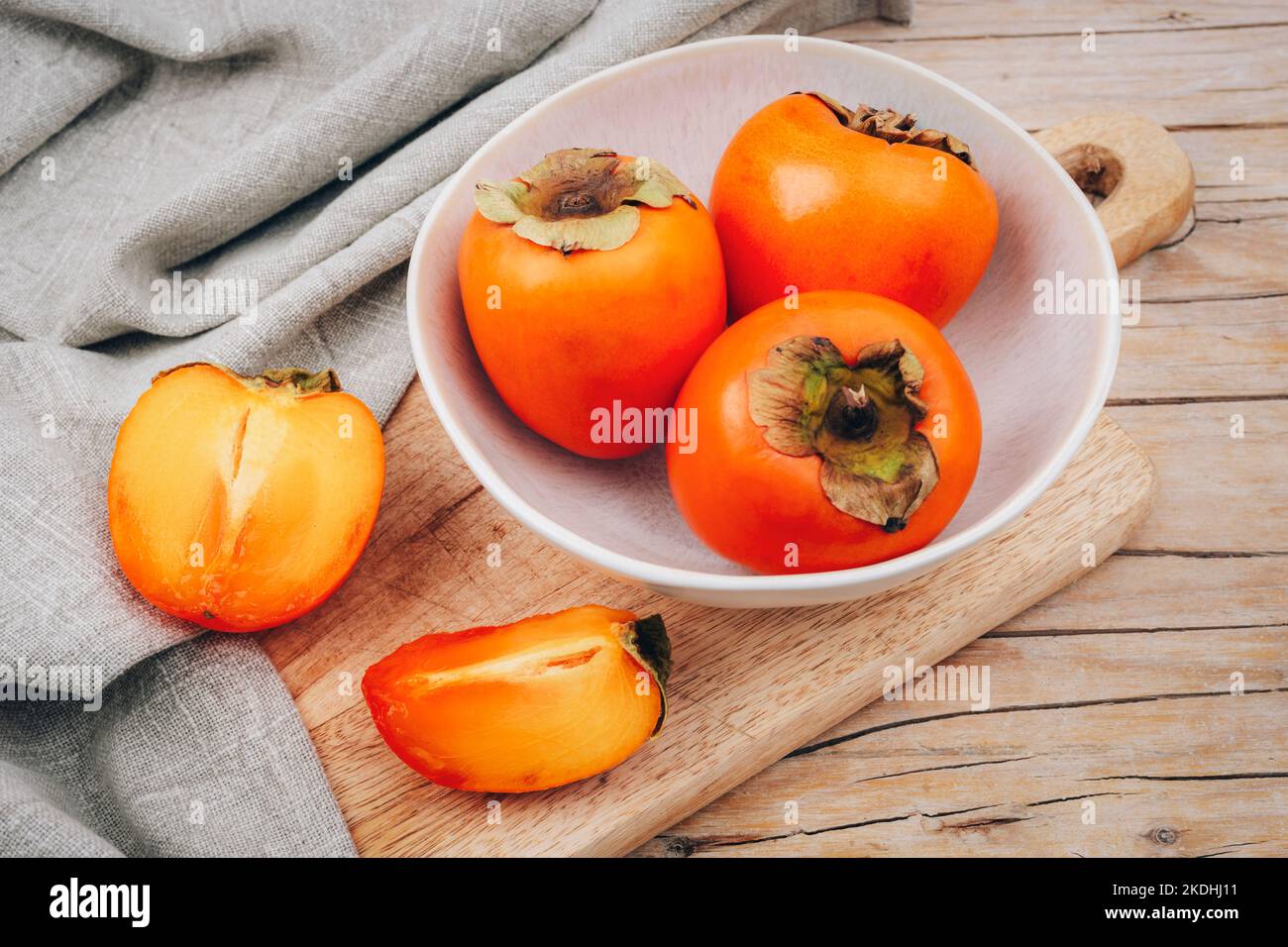 Persimmons frais mûrs dans un bol blanc sur la planche à découper et serviette sur une table en bois. Concept alimentaire végétalien sain. Vue de dessus. Banque D'Images