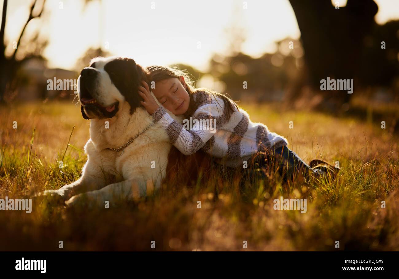 Certaines choses peuvent remplir votre coeur sans essayer. Une petite fille mignonne en cuddling avec son chien pendant qu'ils jouent à l'extérieur. Banque D'Images