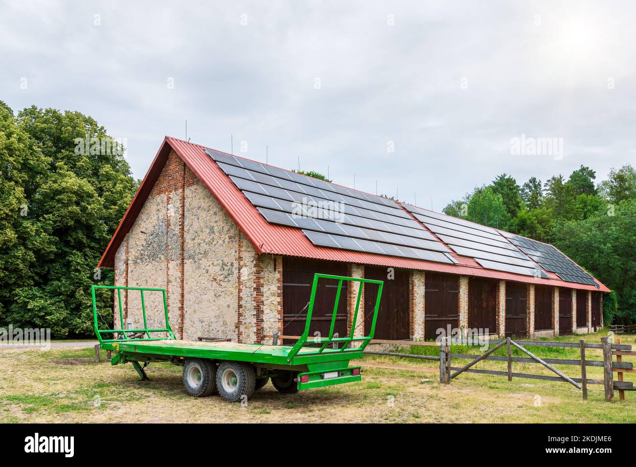 Remorque de ferme verte garée devant une grande grange. Panneaux solaires installés sur le toit de la grange Banque D'Images